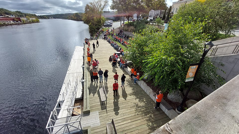 A group of people gathered on a dock by the LaHave River for an event on a sunny day.
